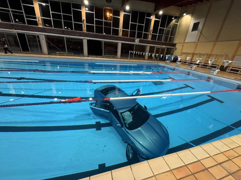 Car submerged in swimming pool at night.
