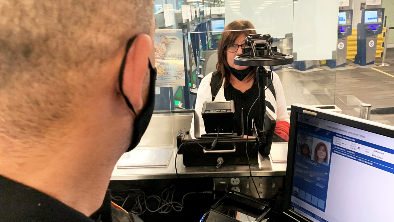 US border control officers processing travelers at an international airport using biometric screening technology