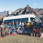 Group in traditional blankets before mountain lodge