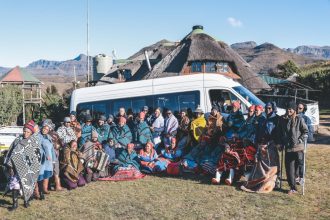 Group in traditional blankets before mountain lodge