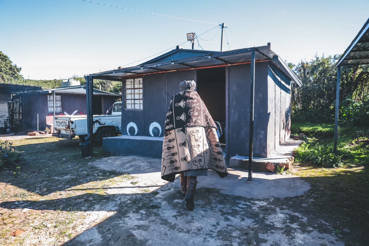 Person in traditional blanket walking towards rural home