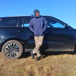 Man leaning against black SUV on grassy field