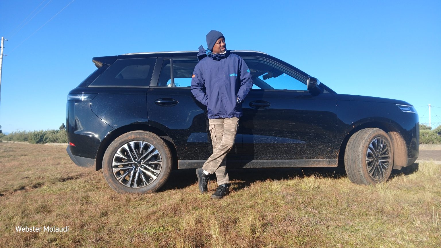 Man leaning against black SUV on grassy field