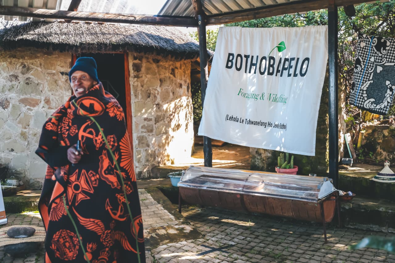 Man in traditional blanket beside Bothobapelo banner