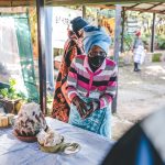 Woman in mask serving cake at outdoor gathering