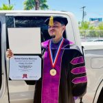 Graduate in regalia holding diploma beside bakkie