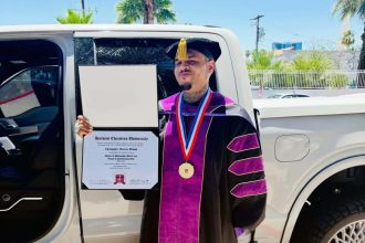 Graduate in regalia holding diploma beside bakkie