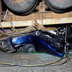 Blue car crushed under large truck trailer