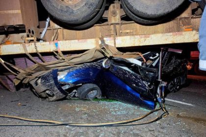 Blue car crushed under large truck trailer