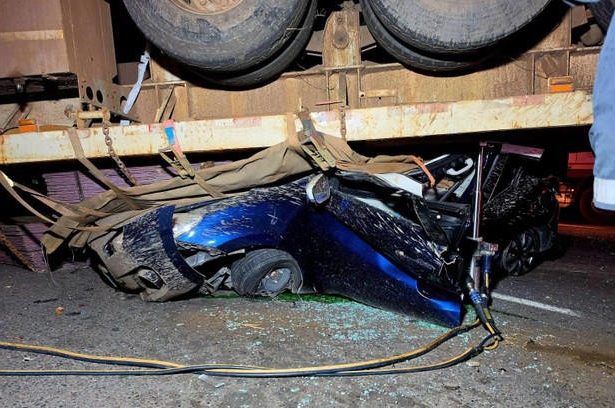 Blue car crushed under large truck trailer