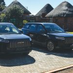 Two black Jaecoo SUVs parked near thatched lodges