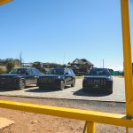 Three black SUVs parked under yellow frame
