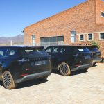 Three black SUVs parked outside brick building