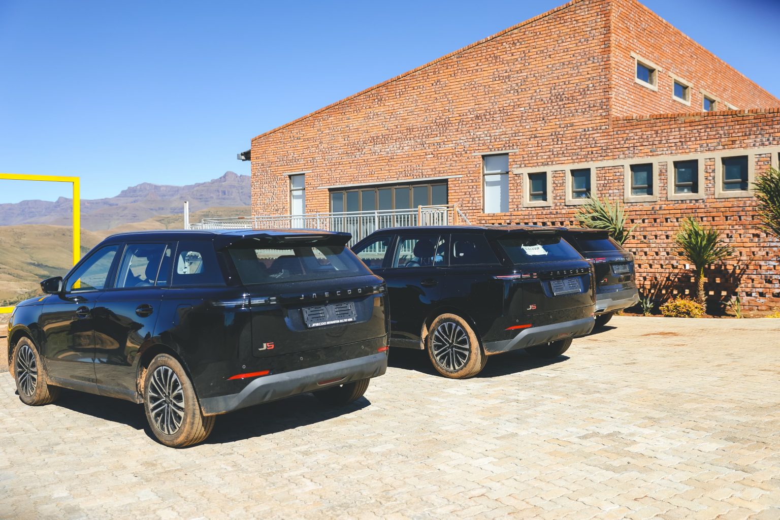 Three black SUVs parked outside brick building