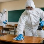Workers disinfecting classroom desks in protective suits
