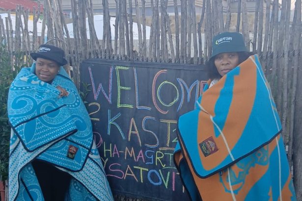 Two women wrapped in blankets beside welcome sign