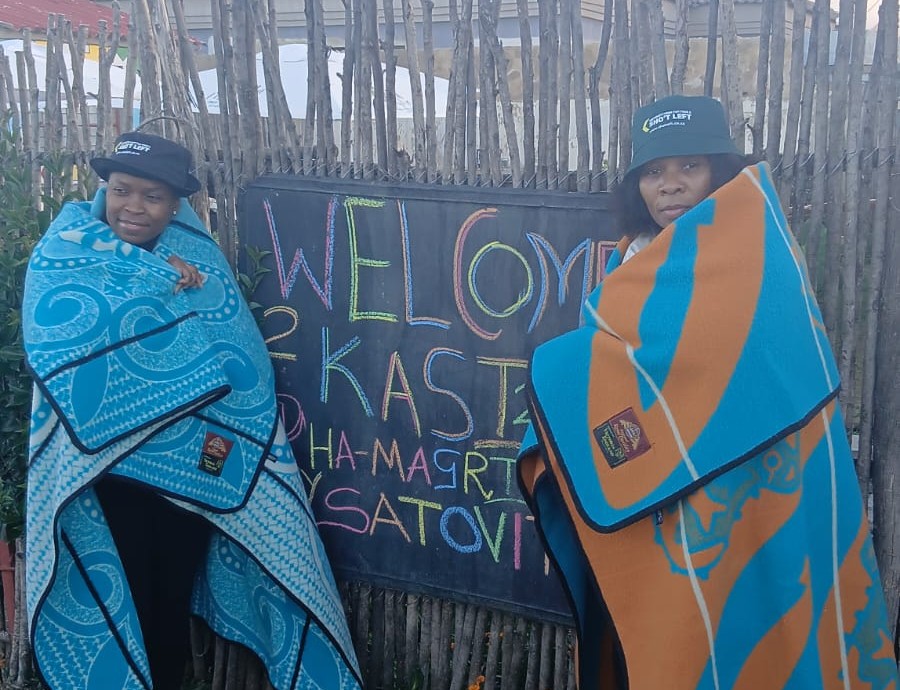 Two women wrapped in blankets beside welcome sign