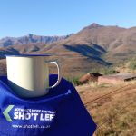 Enamel mug on cap overlooking mountain landscape