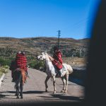 Two riders on horses along rural mountain road