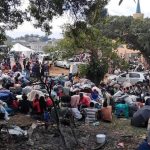 Large crowd gathered outdoors with bags and belongings