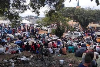 Large crowd gathered outdoors with bags and belongings