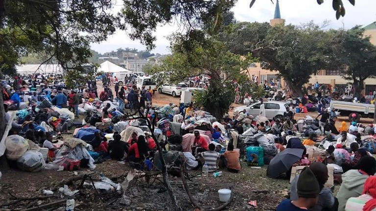 Large crowd gathered outdoors with bags and belongings