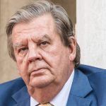 Older man in blue suit with serious expression