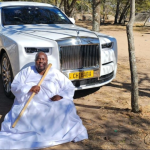 Man in white robe before luxury car