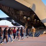 Men boarding large military cargo aircraft via ramp