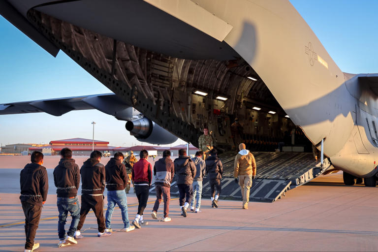 Men boarding large military cargo aircraft via ramp