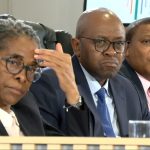 Three officials seated at formal inquiry panel
