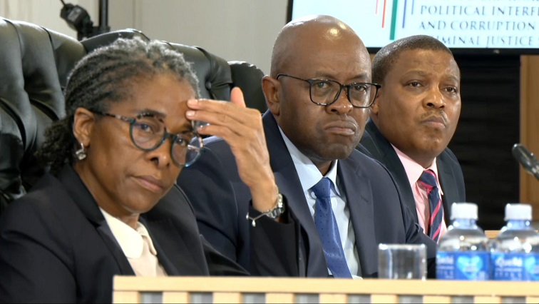 Three officials seated at formal inquiry panel