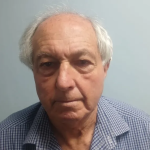 Elderly man in checkered shirt against plain wall