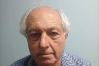 Elderly man in checkered shirt against plain wall