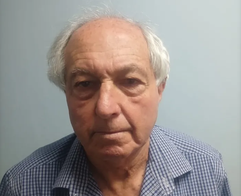 Elderly man in checkered shirt against plain wall