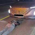 Man lying face down on road in front of SUV.