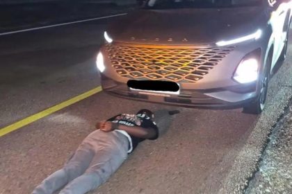Man lying face down on road in front of SUV.