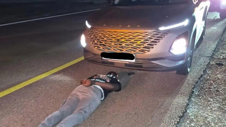 Man lying face down on road in front of SUV.