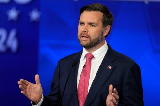 Man in suit speaks with raised hand gestures