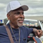 Man in white cap speaking beside a pickup truck