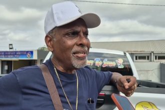 Man in white cap speaking beside a pickup truck