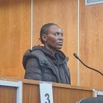 Woman stands at microphone in wood-panelled courtroom