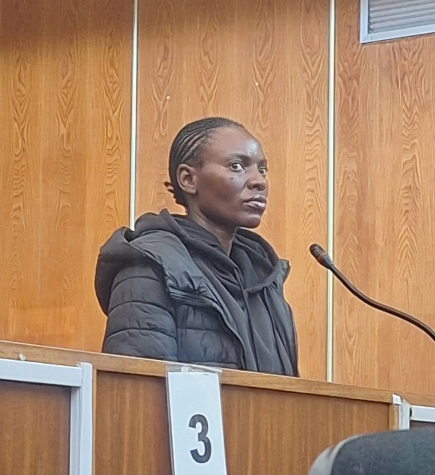 Woman stands at microphone in wood-panelled courtroom