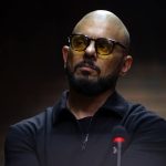 Bald bearded man wearing yellow-tinted glasses at microphone