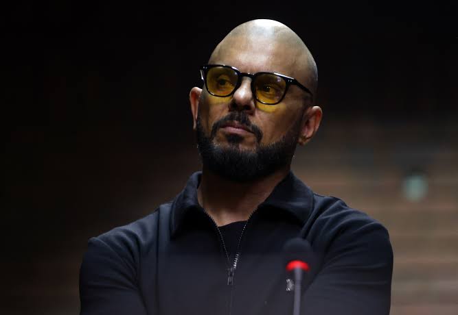 Bald bearded man wearing yellow-tinted glasses at microphone